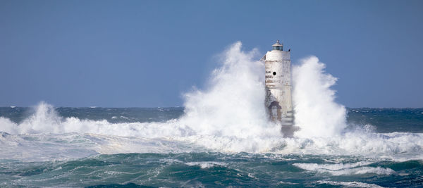 Waves splashing on shore against clear sky