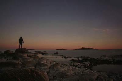 Rear view of man standing on rock at sunset