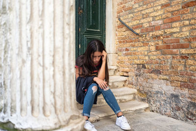 Young woman sitting on stairs near old brick wall