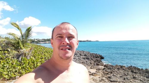 Shirtless man on rocky shore at beach against sky during sunny day