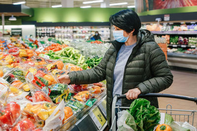 Grocery shopping. middle age woman in protective face mask buying food vegetables in supermarket 