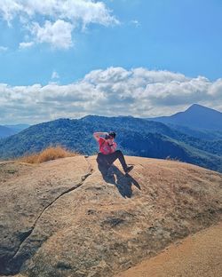 Man sitting on rock against sky