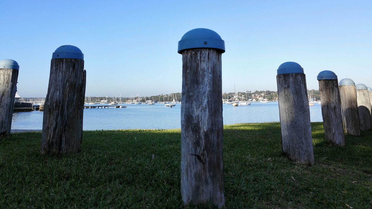 grass, water, clear sky, sea, blue, tranquil scene, tranquility, wooden post, nature, lighthouse, horizon over water, scenics, protection, built structure, day, beauty in nature, sky, safety, architecture, copy space