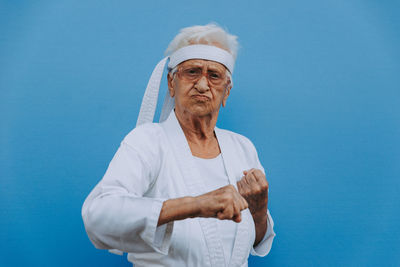 Portrait of senior woman doing karate against blue background