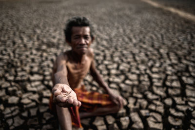 Senior man with hands cupped sitting on cracked land