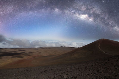 Scenic view of desert against sky milky way above coulds