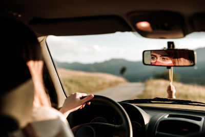 Reflection of woman with protective face mask in car mirror while driving