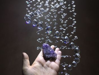 Close-up of hand holding amethyst crystal over brown  background