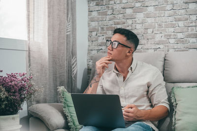 Young woman using laptop while sitting on sofa at home