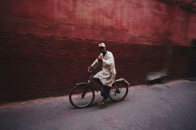 Man riding bicycle on road against wall