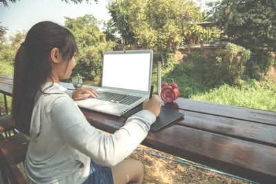 Woman using mobile phone while sitting on tree