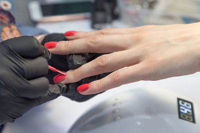 Cropped hands of manicurist applying nail polish on finger of woman