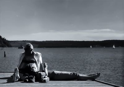 Rear view of man sitting on bench by river