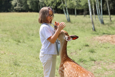 A girl feeding cute spotted deer bambi at petting zoo.