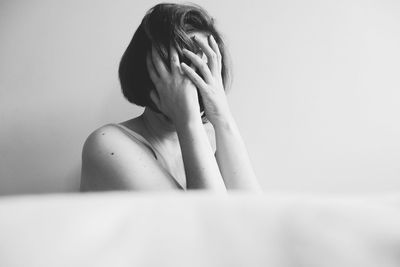 Sad woman covering face with hands against wall