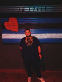 Portrait of young man standing against wall at night