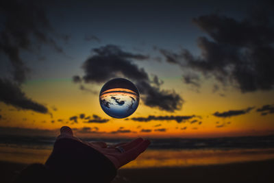 Silhouette man holding ball against orange sky