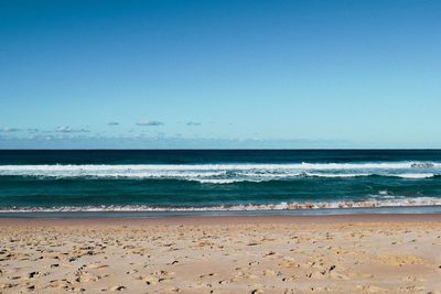 View of calm sandy beach against clear blue sky