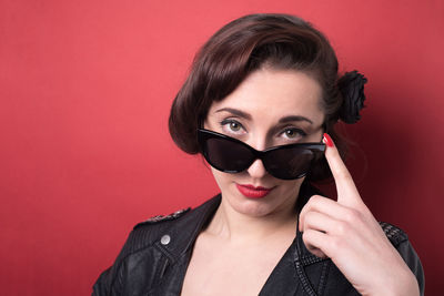 Portrait of young woman adjusting sunglasses against red background