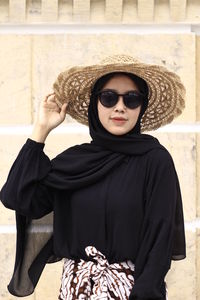 Portrait of woman wearing sunglasses standing against wall