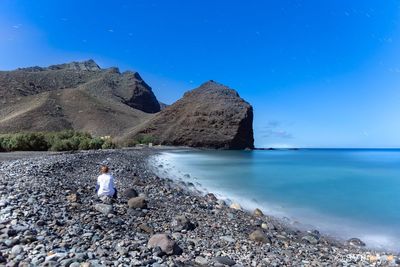 Woman sitting at sea shore against sky