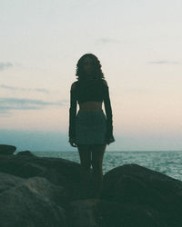 Rear view of woman standing on beach against sky