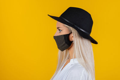 Close-up of woman wearing mask and hat against yellow background