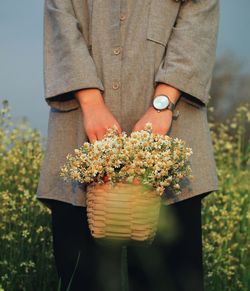 Midsection of person holding flower standing on field