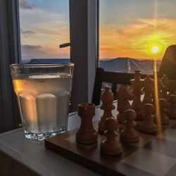 Chess board and drink in glass on table against sky during sunset
