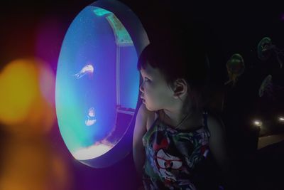 Girl looking at jelly fishes in illuminated tank at aquarium