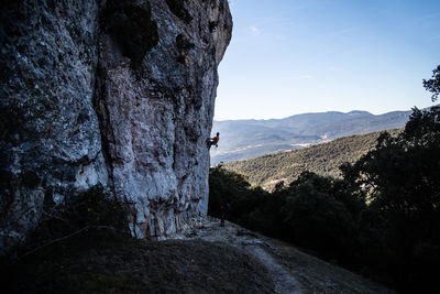 Man climbing on rock formation against sky