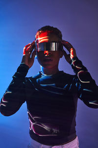 Serious african american female with short hair wearing contemporary vr glasses while standing on purple background in studio with glowing neon lights