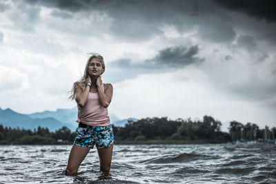 Young woman standing in lake against cloudy sky