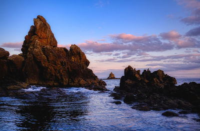 Rock formation in sea against sky during sunset