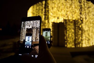 Cropped image of hand photographing illuminated building at night