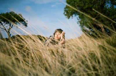 Portrait of woman lying on field amidst grass against sky