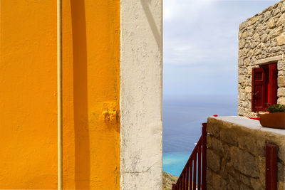 Between a wall in yellow and a gray stone wall looking down at the blue sea 