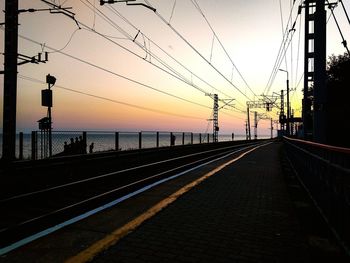 Railroad tracks by sea against sky during sunset