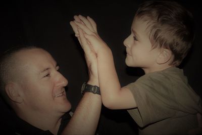 Close-up of father and son high fiving against black background