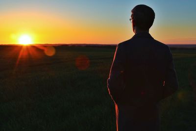 Silhouette man standing on field against sky during sunset