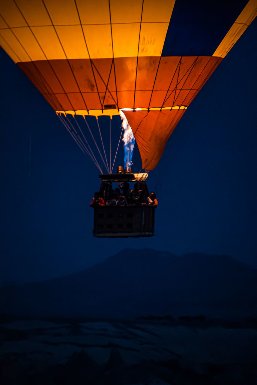 transportation, sky, mode of transportation, illuminated, nature, flying, air vehicle, night, orange color, real people, adventure, mountain, water, sunset, group of people, travel, outdoors, dusk, leisure activity, mid-air