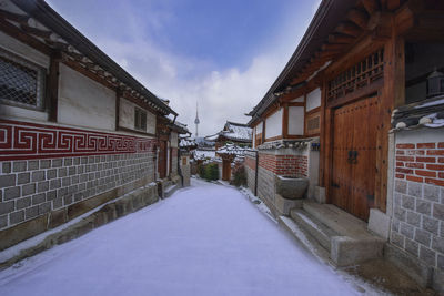 Snow covered footpath amidst buildings in city against sky