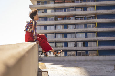 Smiling woman with tousled hair sitting on wall at parking deck