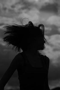 Close-up of silhouette young woman shaking head against cloudy sky during sunset