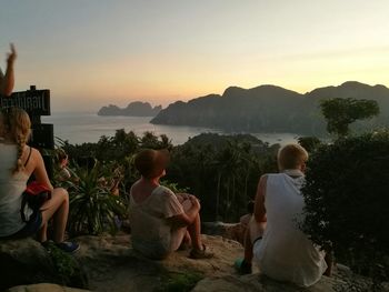 People relaxing on beach against sky during sunset