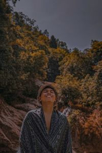 Midsection of young man looking away against trees