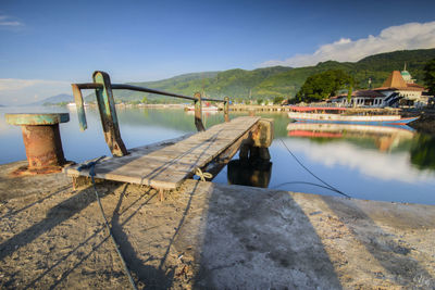 Pier on lake by mountain against blue sky