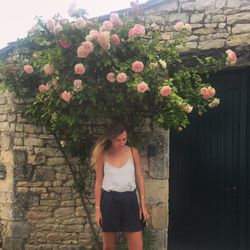 Young woman standing below flowering plant against stone wall