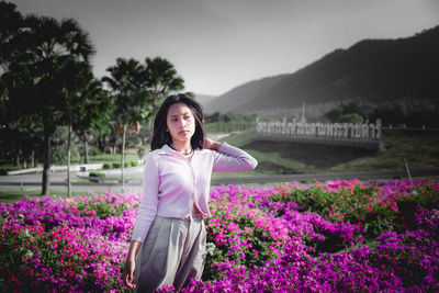 Portrait of smiling young woman standing by purple flowering plants