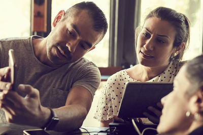 Man using smart phone while women looking in cafe